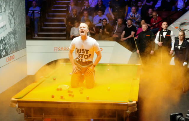 A Just Stop Oil protester jumps on the table and throws orange powder during the match between Robert Milkins against Joe Perry during day three of the Cazoo World Snooker Championship at the Crucible Theatre, Sheffield. Picture date: Monday April 17, 2023. PA Photo. See PA Story SNOOKER World. Photo credit should read: Mike Egerton/PA Wire. RESTRICTIONS: Use subject to restrictions. Editorial use only, no commercial use without prior consent from rights holder.